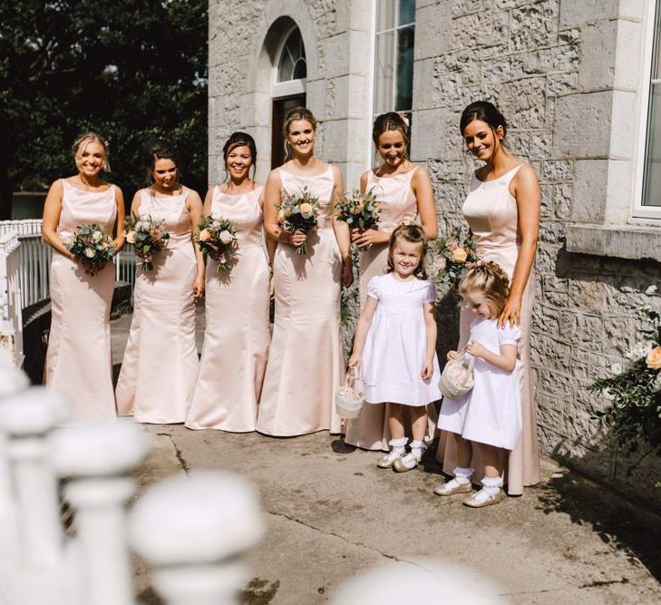 Peachy pink bridesmaid dresses with flower girls wearing white dresses at Wales wedding venue