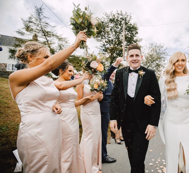 Bride and groom confetti exit with bridesmaids wearing peachy pink dresses teamed with rose floral bouquets