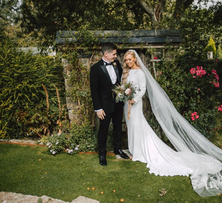 Bride and groom at Wales wedding venue wearing split front dress and lace tipped long veil