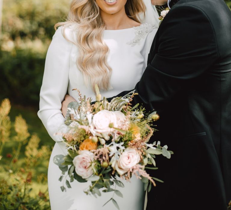 Bride and groom embrace at Welsh celebration with peachy pink floral bouquet