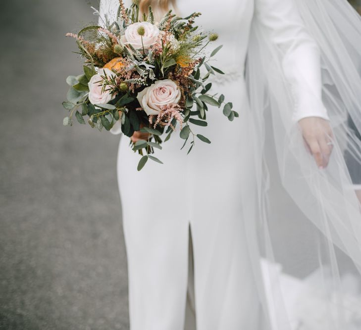 Bride and groom embrace at Welsh celebration with peachy pink floral bouquet and split front bridal dress