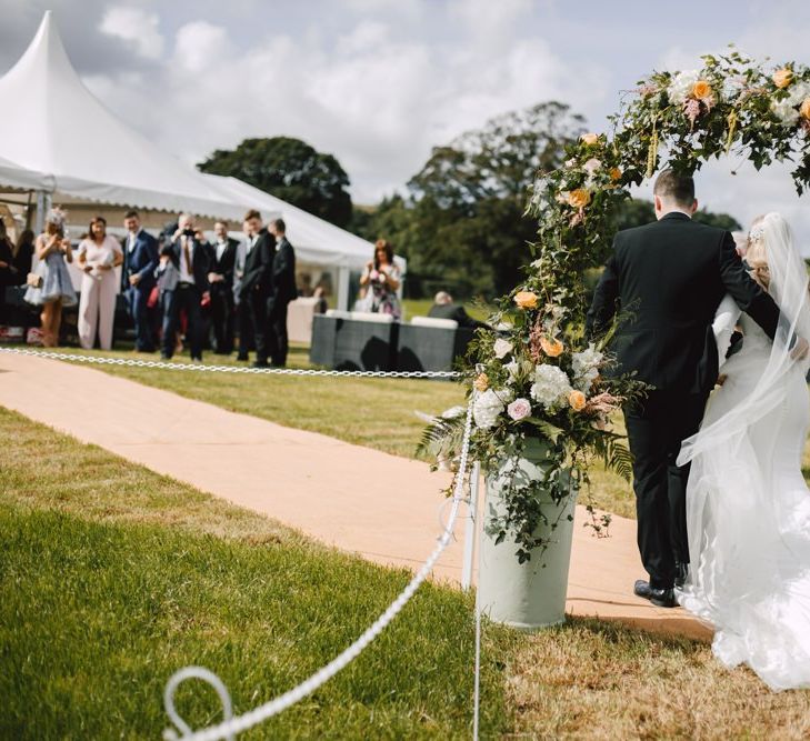 Bride and groom arrive at marquee reception with floral arch display