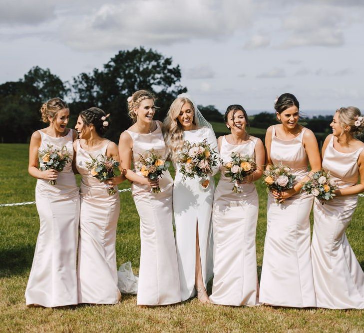 Bride and her bridesmaids wearing peachy pink bridesmaid dresses and floral bouquets at Wales wedding venue