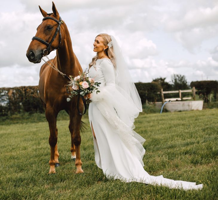 Bride wearing long lace tipped veil with her horse at marquee reception with equestrian touches