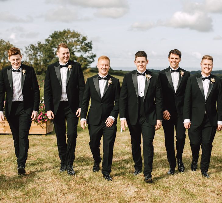 Groom and his groomsmen wearing black tie at marquee reception with blush and gold detailing