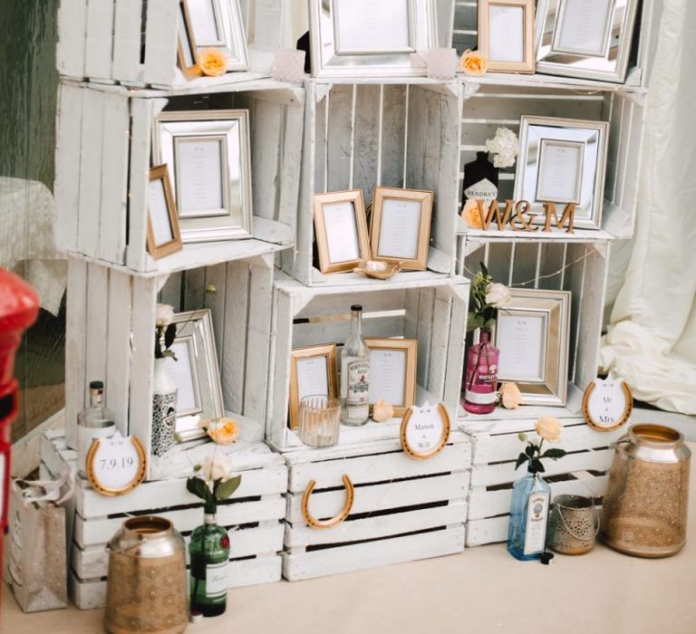 Painted crates with picture frames and gold painted stirrups for personal table plan at Wales wedding venue