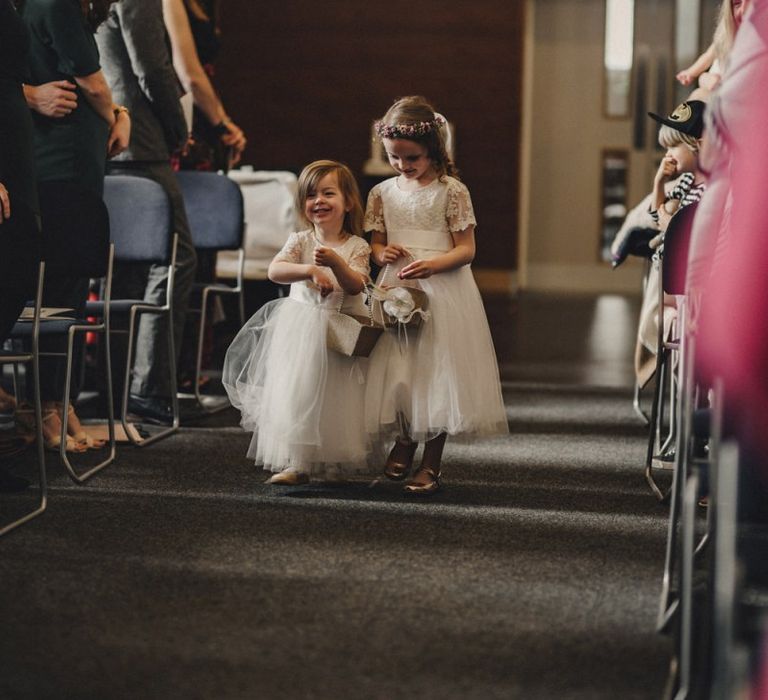 Flower girls in white dresses walking down the aisle