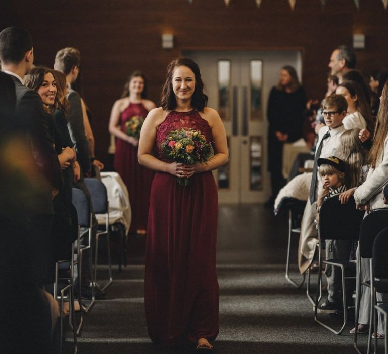 Bridesmaid in red halterneck dress walking down the aisle