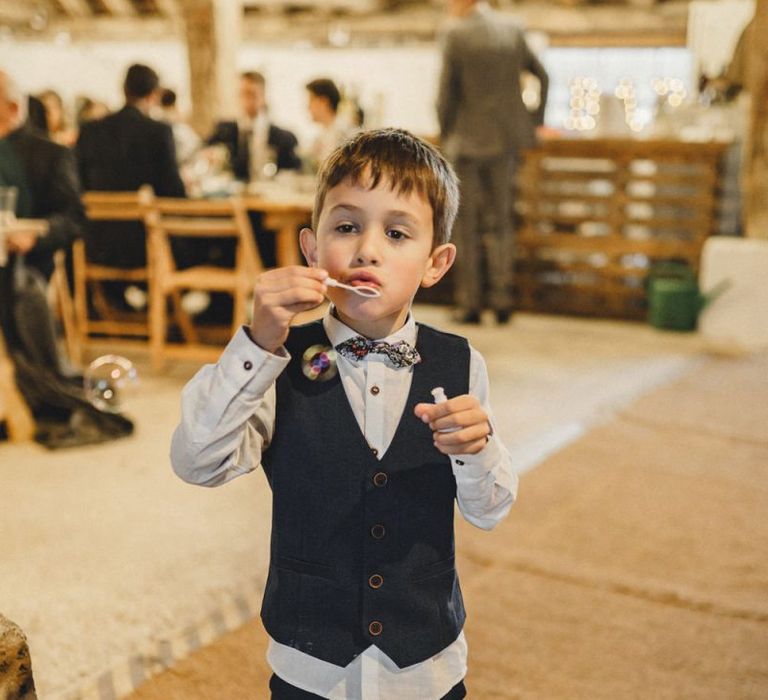 Page boy blowing bubbles at rustic wedding