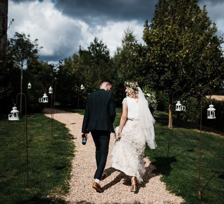 Bride in Halfpenny London Swan Tulle Petal Skirt and Flower Crown and Groom in Wool Suit Walking Through the Courtyard