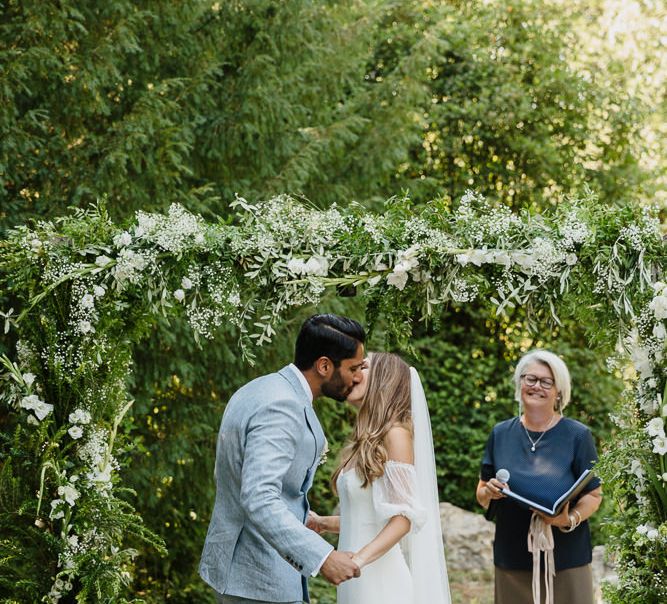 Bride and groom with celebrant at an outdoor wedding in Provence with bride wearing off the shoulder wedding dress