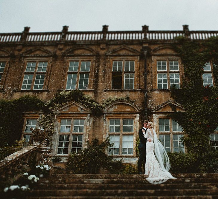 Bride in Vintage Lace Tara Lauren Wedding Dress and Groom in Black Tie Suit Standing Front of Brympton House Wedding Venue