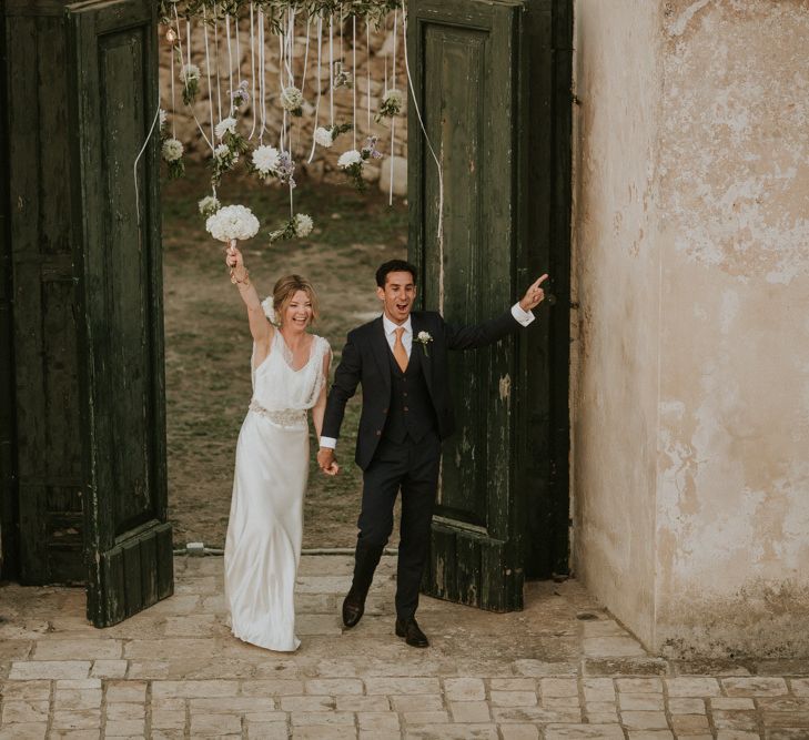 Bride in Halfpenny London Wedding Dress and Groom in Navy Blue Suit Entering the Wedding Breakfast