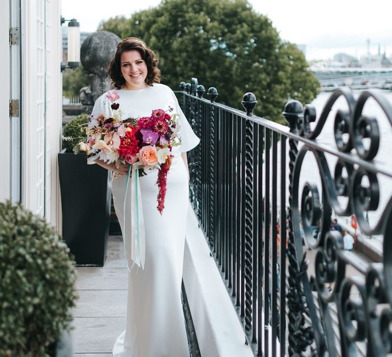 Bride in Halfpenny London Dress with Cowl Back and Half Length Sleeves | Colourful Deconstructed Bridal Bouquet of Red and Pink Flowers with Trailing Ribbon | Tilly Thomas Lux Headband | Meringue Kisses &amp; Colourful Wedding Flowers &amp; Stationery for a London Wedding at The Globe | Miss Gen