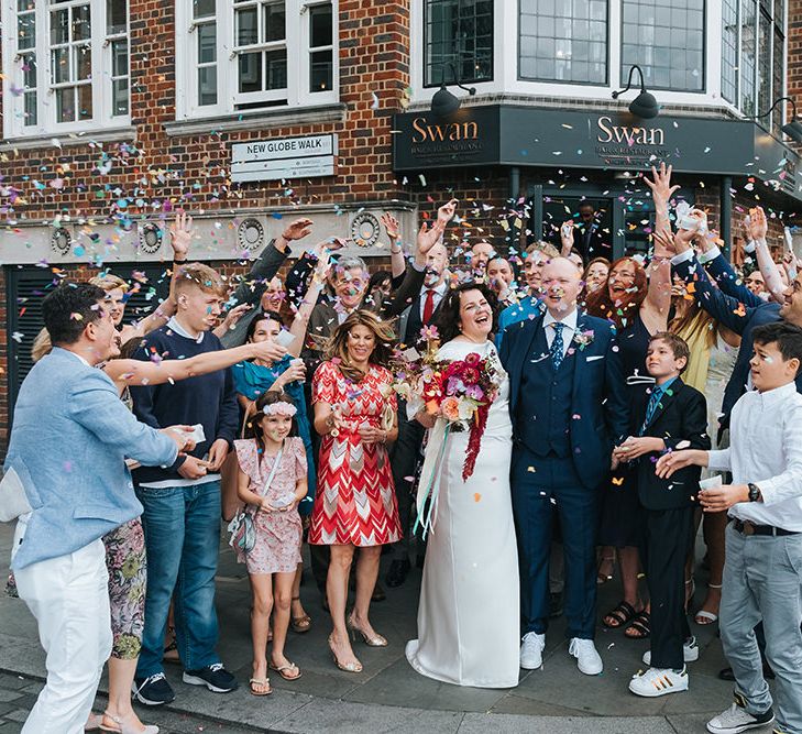 Bride in Halfpenny London Dress with Cowl Back and Half Length Sleeves | Colourful Deconstructed Bridal Bouquet of Red and Pink Flowers with Trailing Ribbon | Tilly Thomas Lux Headband | Groom in Blue Three-Piece Suit and White Trainers | Wedding Ceremony at The Swan at The Globe | Meringue Kisses &amp; Colourful Wedding Flowers &amp; Stationery for a London Wedding at The Globe | Miss Gen