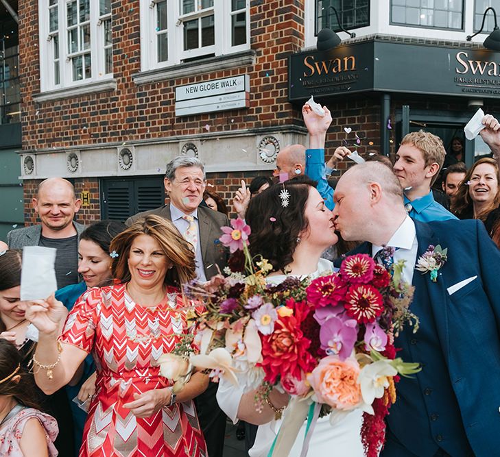 Bride in Halfpenny London Dress with Cowl Back and Half Length Sleeves | Colourful Deconstructed Bridal Bouquet of Red and Pink Flowers with Trailing Ribbon | Tilly Thomas Lux Headband | Groom in Blue Three-Piece Suit and White Trainers | Wedding Ceremony at The Swan at The Globe | Meringue Kisses &amp; Colourful Wedding Flowers &amp; Stationery for a London Wedding at The Globe | Miss Gen