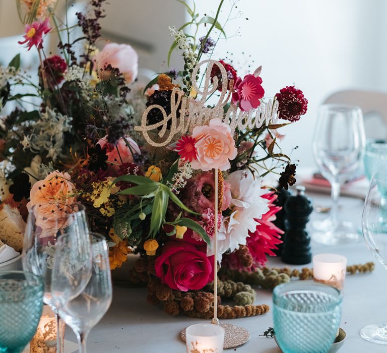 Sparkly Gold Table Sign | Colourful Floral Centrepiece | Tea Light Holders with Gold Glitter Detail | Blue Wine Glasses | Meringue Kisses &amp; Colourful Wedding Flowers &amp; Stationery for a London Wedding at The Globe | Miss Gen