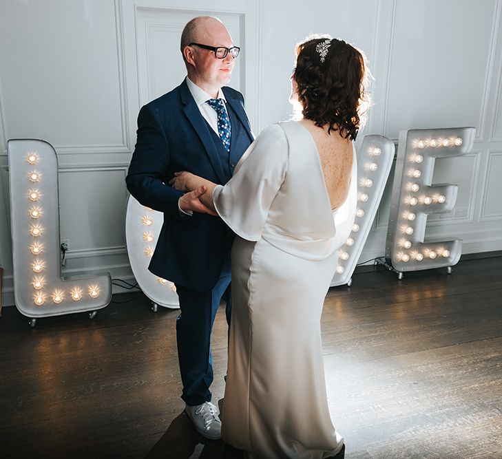 Bride in Halfpenny London Dress with Cowl Back and Half Length Sleeves | Tilly Thomas Lux Headband | Groom in Blue Three-Piece Suit and White Trainers | Love Letter Lights | First Dance at The Swan at The Globe | Meringue Kisses &amp; Colourful Wedding Flowers &amp; Stationery for a London Wedding at The Globe | Miss Gen