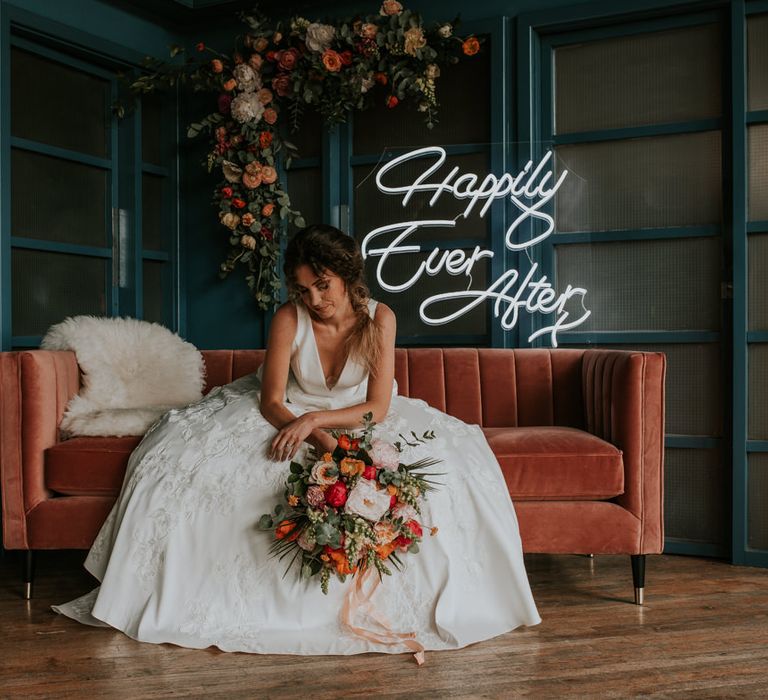 Bride Sitting on Velvet Sofa with Neon 'Happily Ever After ' Sign Backdrop