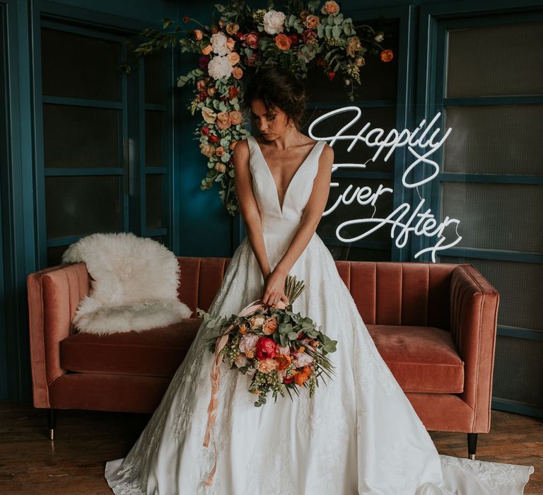 Bride Standing in Front of a Velvet Sofa with Neon 'Happily Ever After ' Sign Backdrop