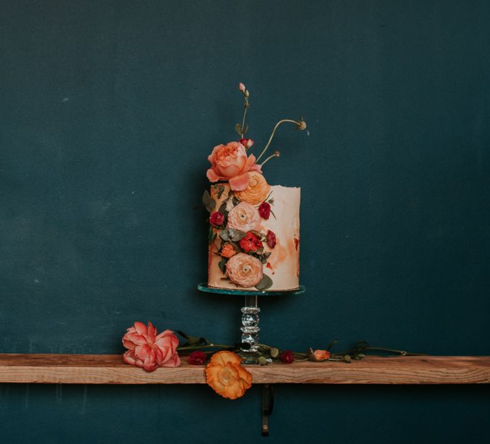 Tall Single Tier Wedding Cake Decorated with Flowers in Glass Cake Stand by a Neon Sign