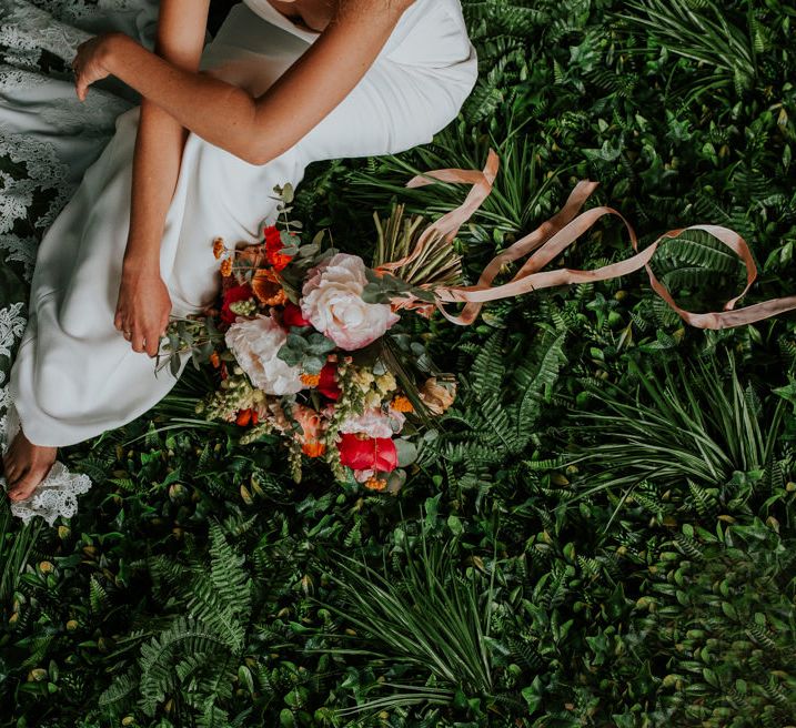 Bride Sitting on The Grass Next to Her Bright Bouquet Showing Off her Lace Wedding Dress Train