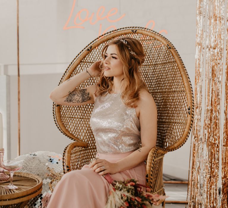 Bridesmaid sitting in a peacock chair in a blush pink and silver dress