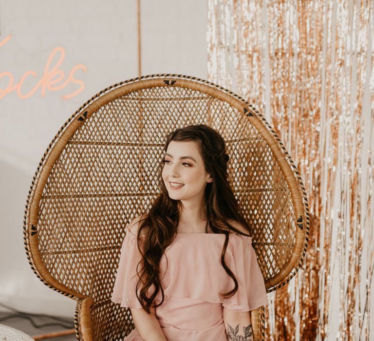 Bridesmaid in a blush pink dress sitting in a peacock chair