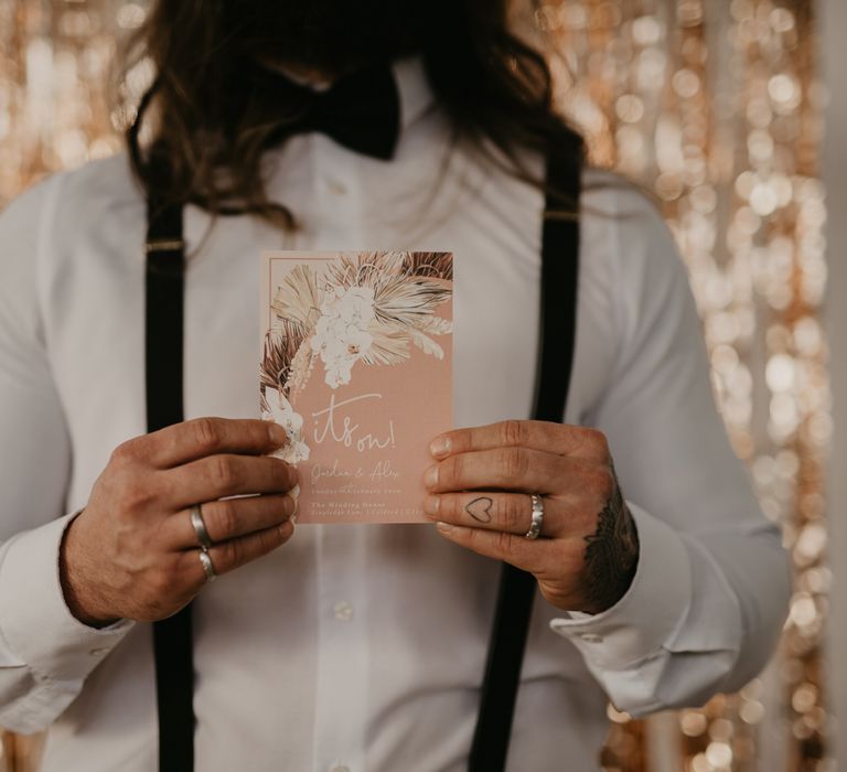 Groom holding a blush pink wedding invitation