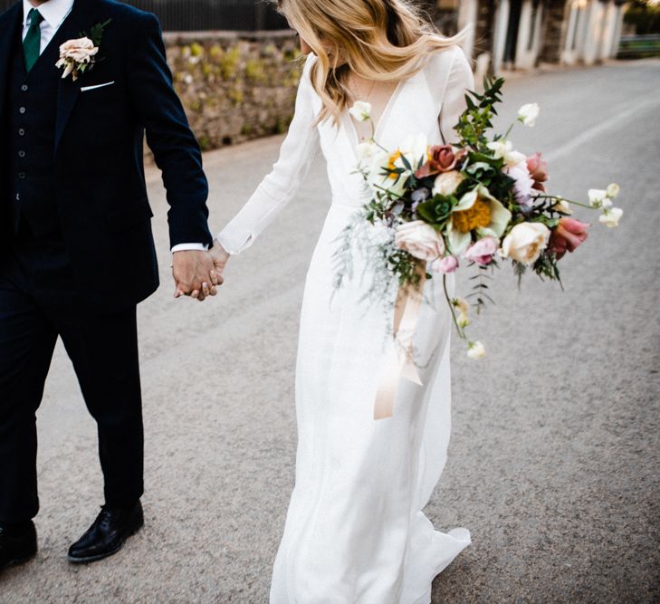 Bride in Andrea Hawkes Wedding Dress and Groom in Navy Suit Holding Hands