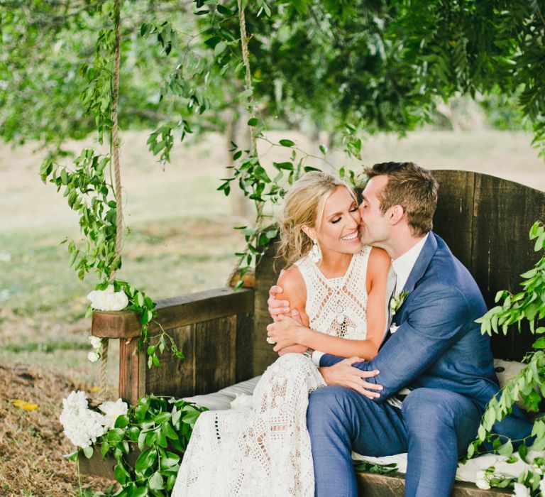 Bride in Lace Rue De Seine Wedding Dress and Groom in Blue Suit  Embracing on the swing