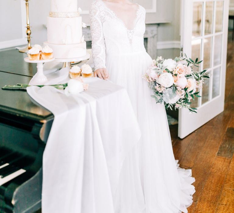 Bride in Lace Wedding Dress Standing Next to Elegant Wedding Cake