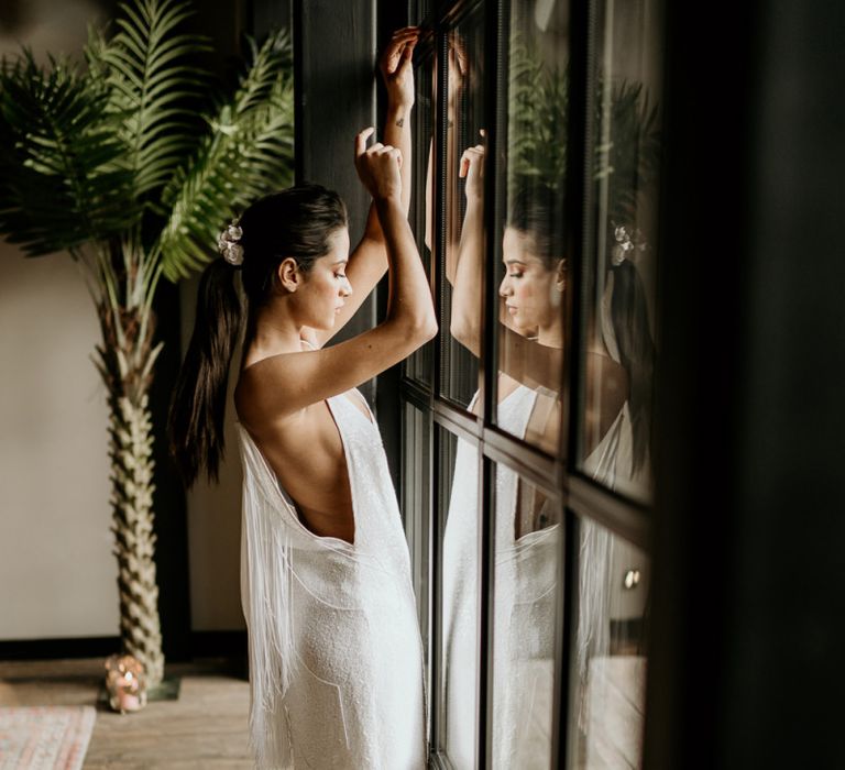 Bride in Minimalist Wedding Dress with Fringe Back Detail Standing at a Window