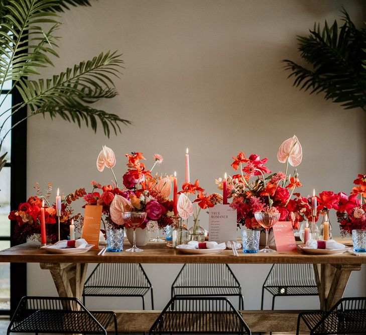 Red and Pink Wedding Flower Table Decor with Taper Candles, Coloured Glasses and Modern Stationery