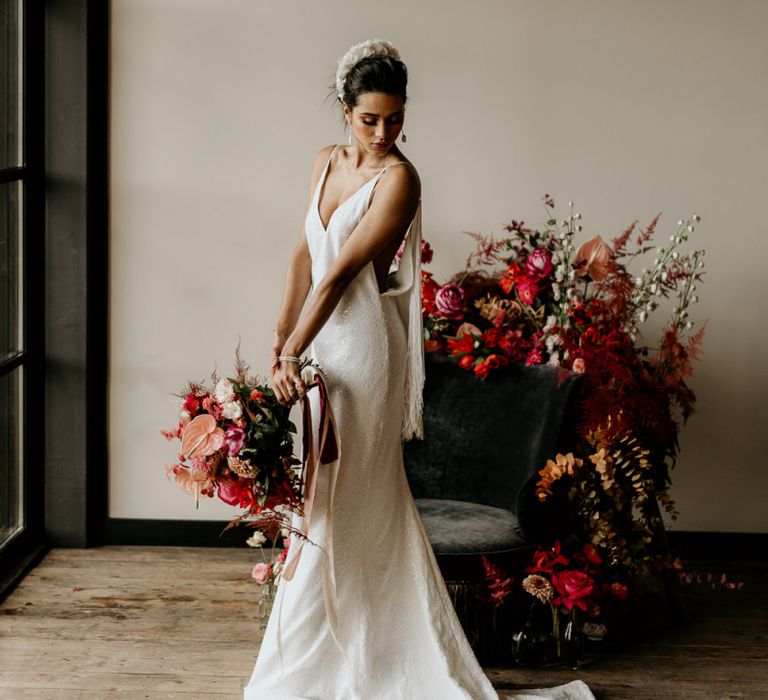 Bride in Minimalist Wedding Dress with Spaghetti Straps and White Headdress Holding a Red and Pink Tropical Bridal Bouquet