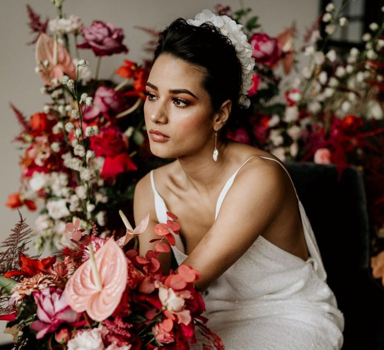 Bride in Minimalist Wedding Dress with Spaghetti Straps and White Headdress Holding a Red and Pink Bridal Bouquet