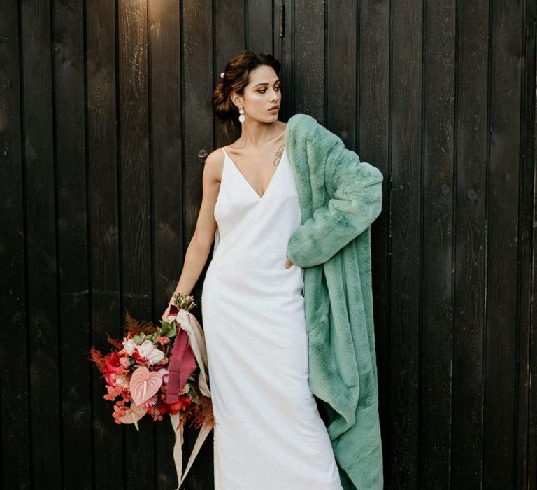 Modern Bride in Minimalist Wedding Dress and Blue Teddy Coat Holding a Pink and Red Bouquet with Anthurium Flower Stems