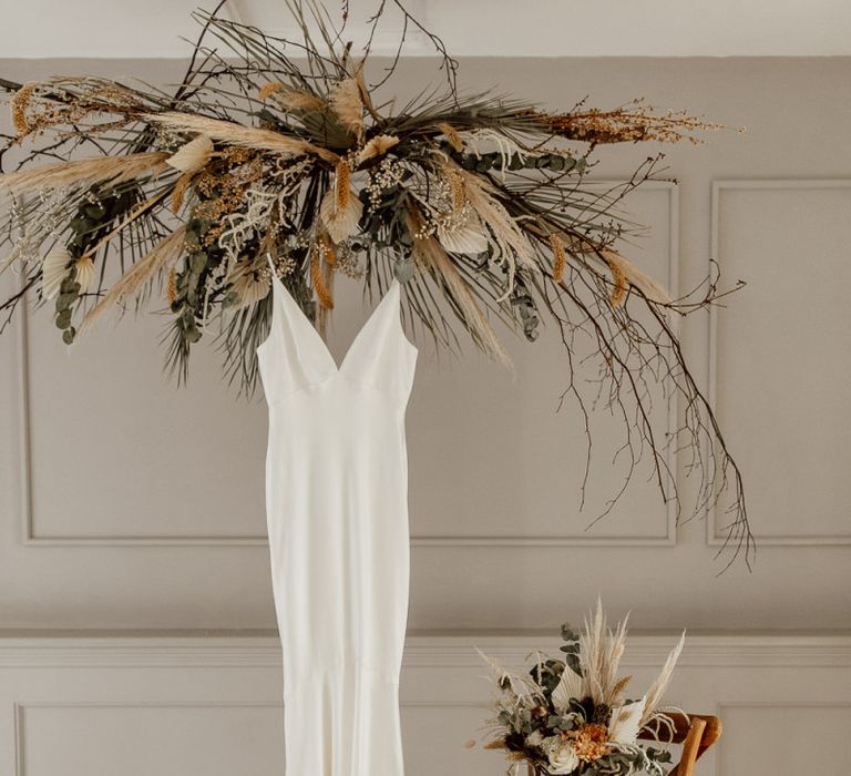 Minimalist Wedding Dress Hanging Under a Dried Flower Installation