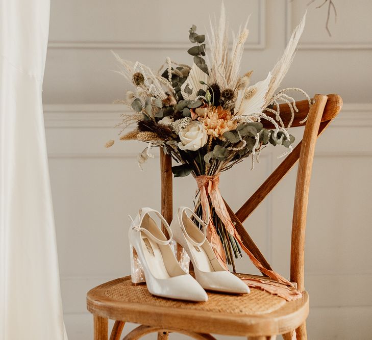 Bridal Shoes and Dried Flower Bouquet Resting on a Wooden Chair