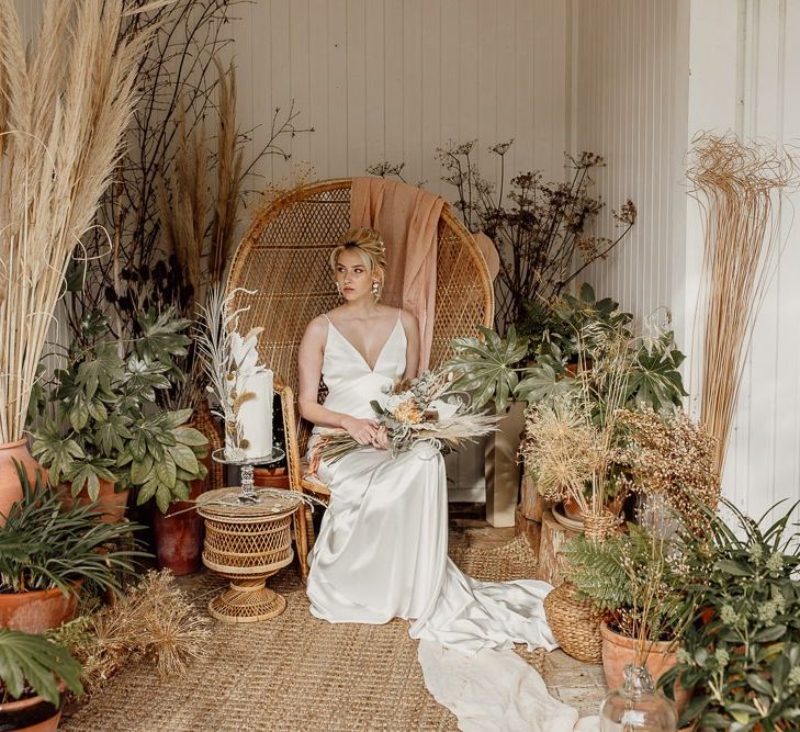 Modern Bride Sitting on a Wicker Peacock Chair Surrounded by Potted Plants