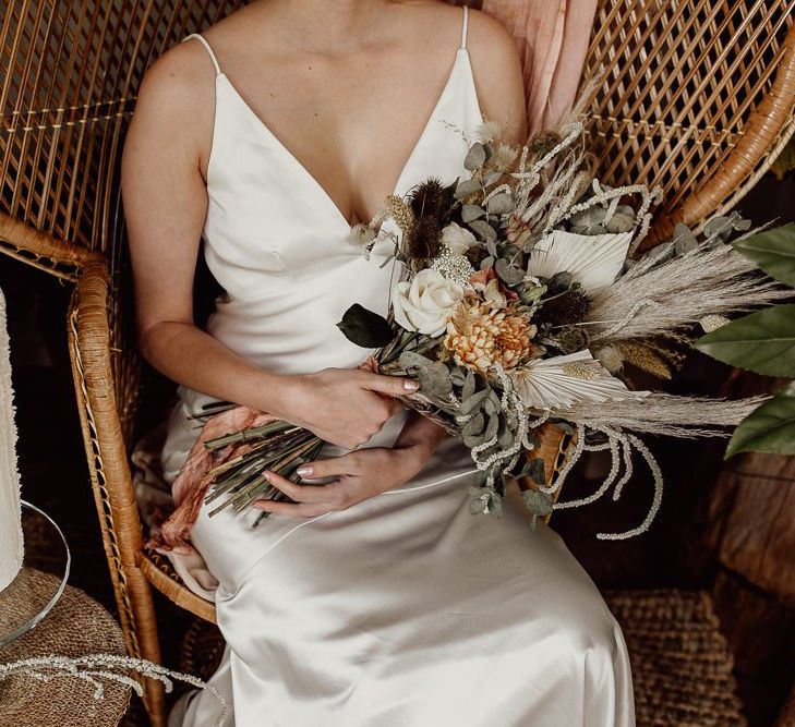 Bride in Minimalist Satin Wedding Dress Sitting on a Peacock Chair Holding Her Bouquet