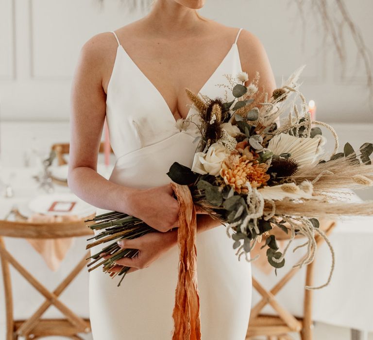 Bride in Minimalist Wedding Dress with Plunging Neckline Holding a Wedding Bouquet Tied with Ribbon