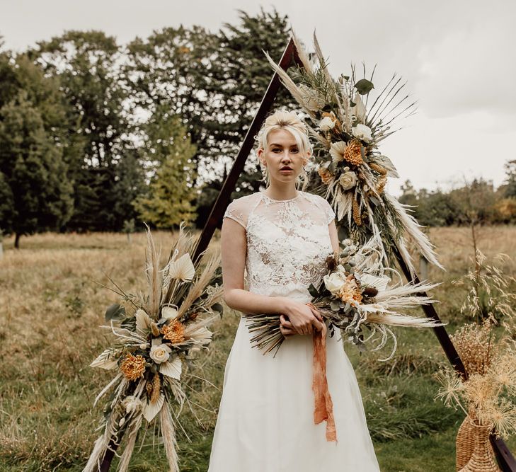 Boho Bride Standing in Front of a Triangle Frame Altar Decorated with Dried Flowers