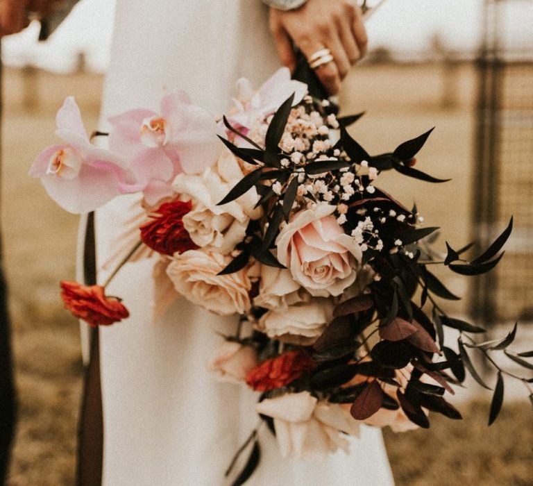 Pink and red wedding bouquet with roses, orchids and foliage