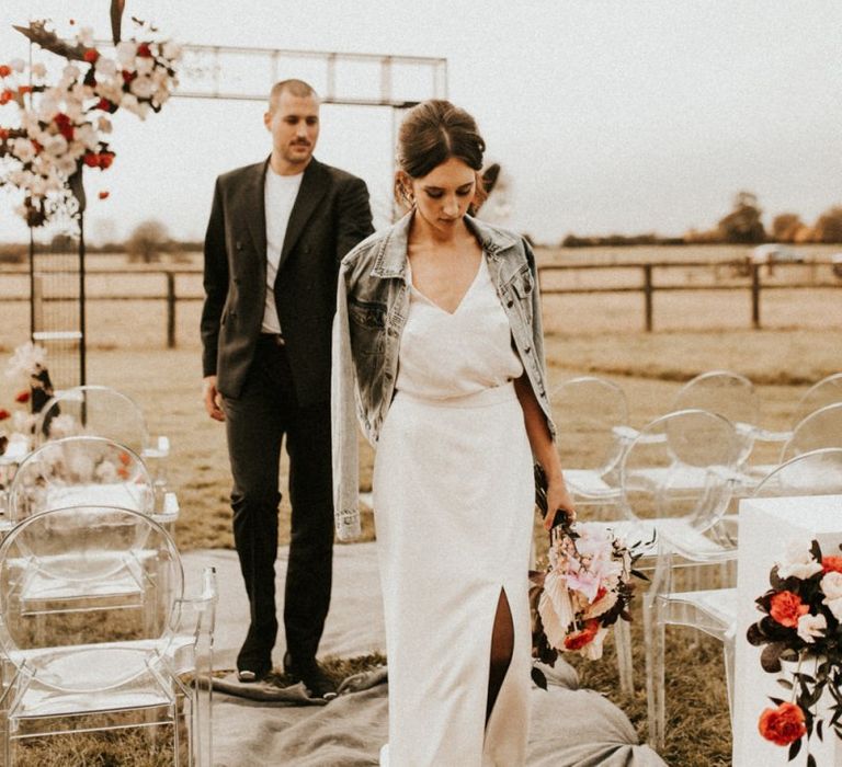 Stylish bride in fitted wedding dress with front slit and denim jacket