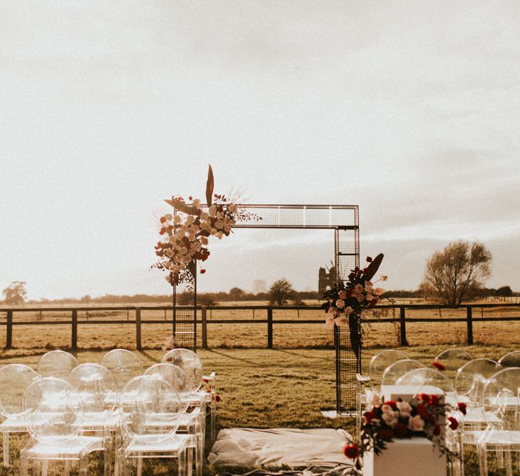 Outdoor wedding ceremony at Godwick Great Barn with wire frame altar and ghost chairs