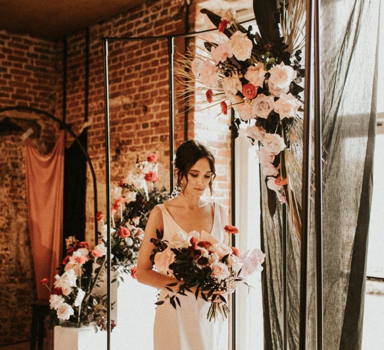 Bride in minimalist dress standing under a metal frame