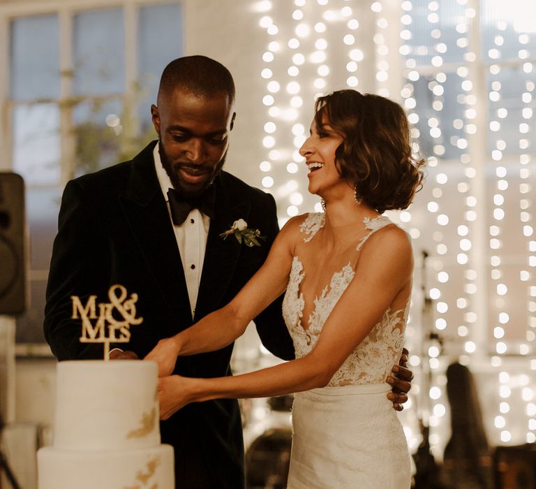 Cutting the Cake. Bride wears dress by Pronovias. Groom wears green velvet blazer from Gieves &amp; Hawkes in this Green And White Luxe, City Wedding. Photography by The Curries.