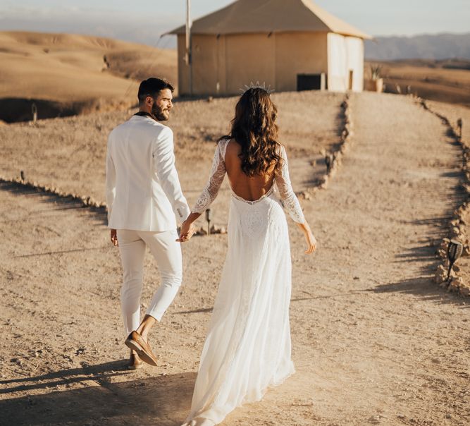 Bride in Grace Loves Lace Wedding Dress and Groom in White Suit Holding Hands