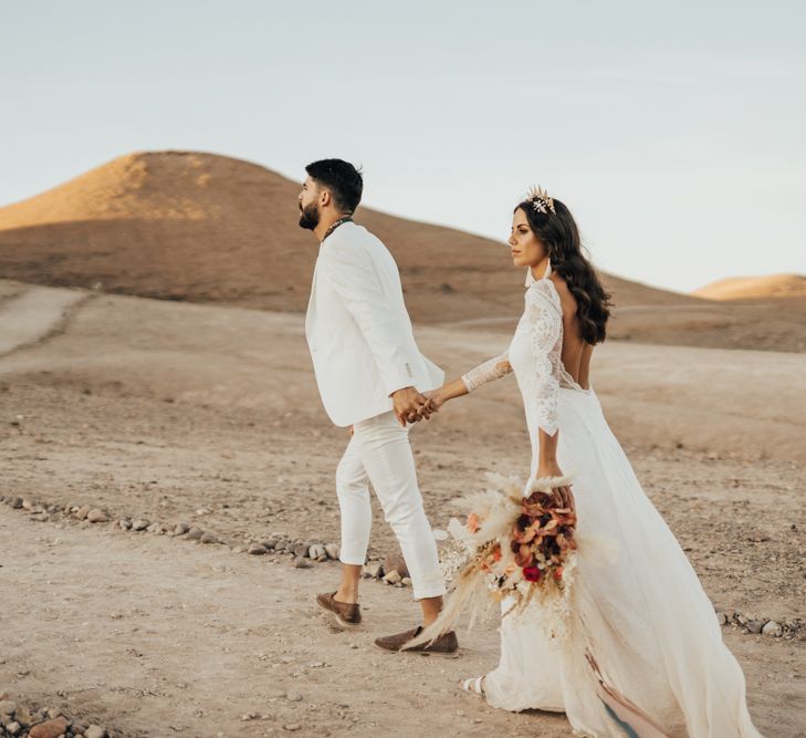 Bride and groom walking through the desert at their Moroccan wedding